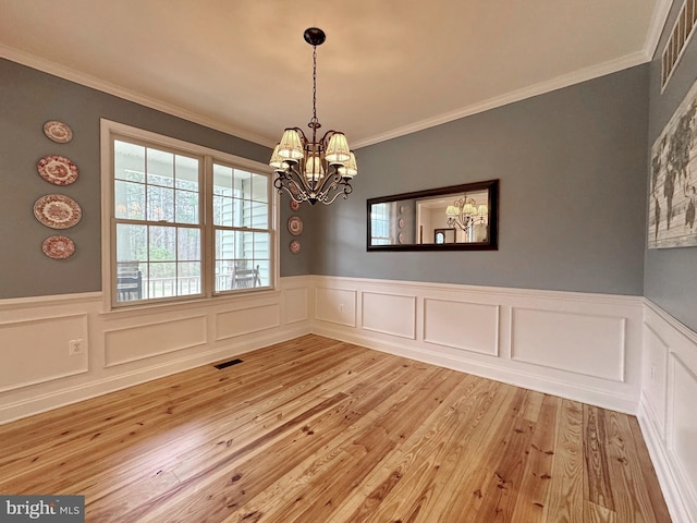 unfurnished dining area with wainscoting, wood finished floors, visible vents, and a chandelier