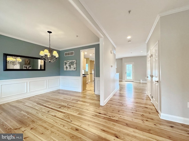 unfurnished dining area with a chandelier, visible vents, light wood-style floors, and a wainscoted wall