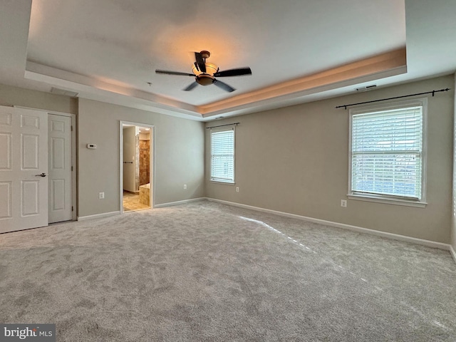 unfurnished bedroom featuring ensuite bathroom, carpet, a raised ceiling, and baseboards