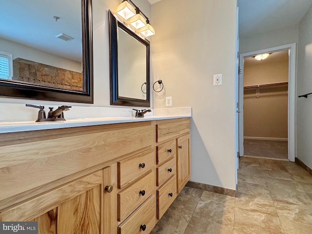 full bath featuring a walk in closet, double vanity, baseboards, and a sink