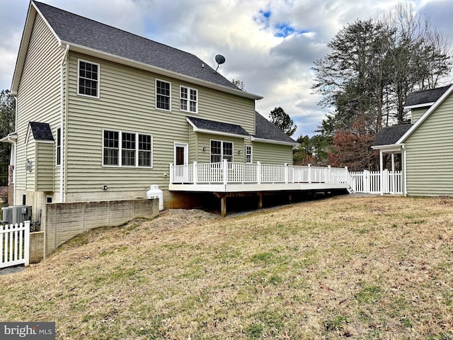 rear view of property with central AC unit, fence, roof with shingles, a wooden deck, and a yard