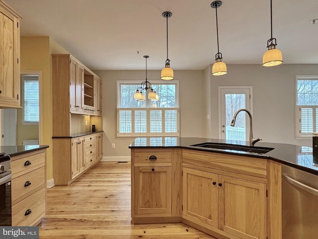 kitchen with stainless steel appliances, light brown cabinetry, a sink, decorative light fixtures, and light wood-type flooring