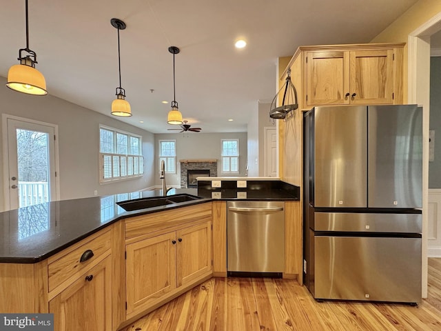 kitchen featuring a sink, a stone fireplace, light wood-style floors, appliances with stainless steel finishes, and decorative light fixtures