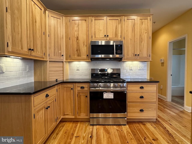 kitchen with dark countertops, light wood finished floors, backsplash, baseboards, and stainless steel appliances