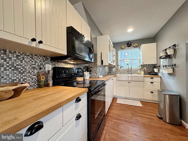 kitchen featuring light wood finished floors, a sink, black appliances, wood counters, and backsplash