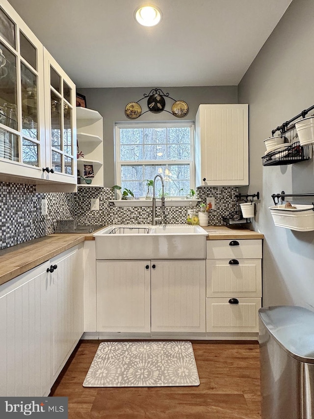 kitchen with dark wood finished floors, open shelves, a sink, glass insert cabinets, and tasteful backsplash