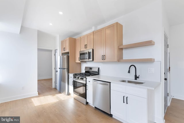 kitchen featuring open shelves, stainless steel appliances, light countertops, a sink, and light wood-type flooring