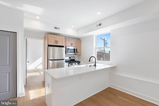 kitchen featuring stainless steel appliances, a sink, light wood-style floors, light countertops, and light brown cabinetry