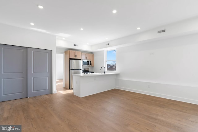 kitchen featuring light wood finished floors, a peninsula, stainless steel appliances, light countertops, and light brown cabinetry