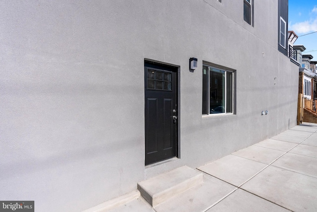 view of exterior entry featuring stucco siding and a patio