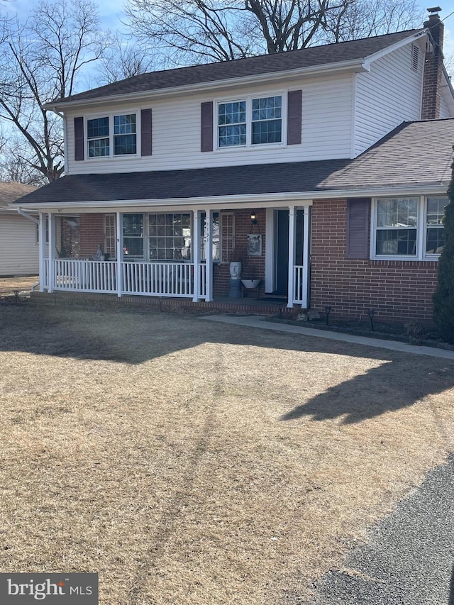 traditional-style house featuring brick siding, covered porch, and a chimney