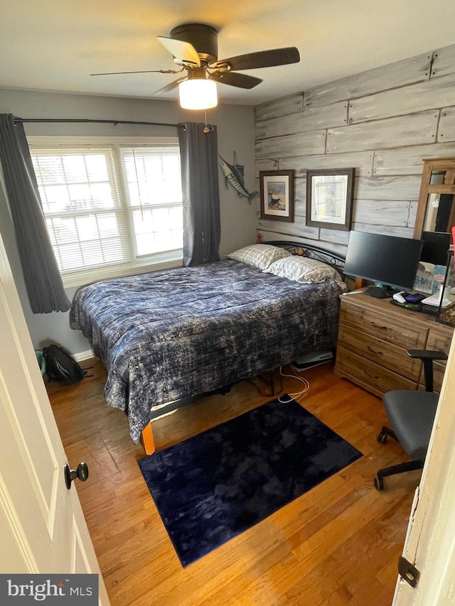 bedroom featuring ceiling fan, wood walls, and wood finished floors