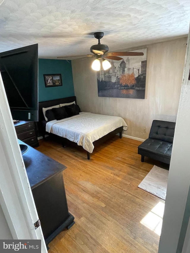 bedroom with ceiling fan, a textured ceiling, baseboards, and wood finished floors