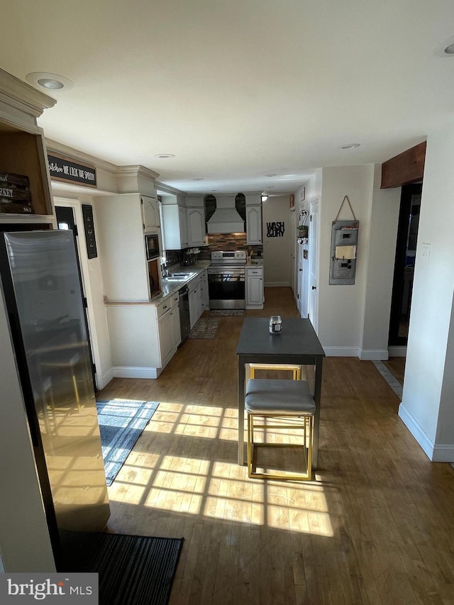 kitchen featuring dark countertops, custom range hood, stainless steel appliances, and wood finished floors