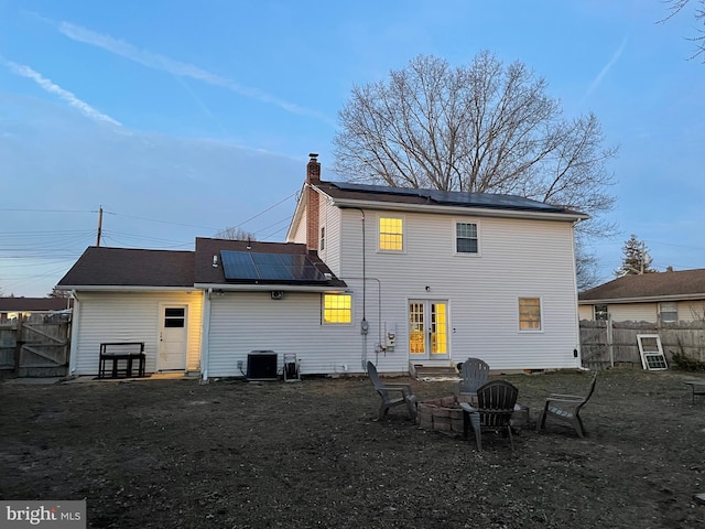 back of property featuring french doors, a chimney, solar panels, an outdoor fire pit, and fence