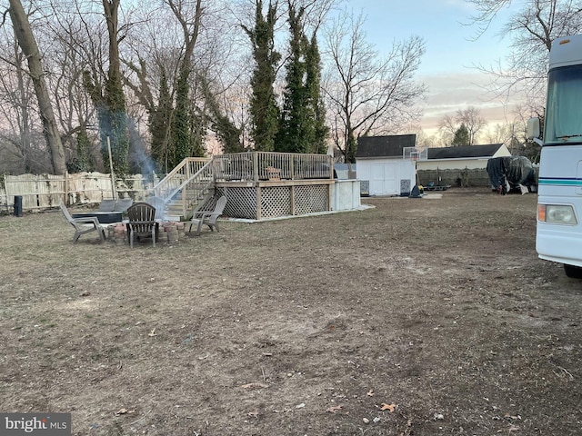 yard at dusk featuring an outbuilding, fence, stairs, a wooden deck, and a shed