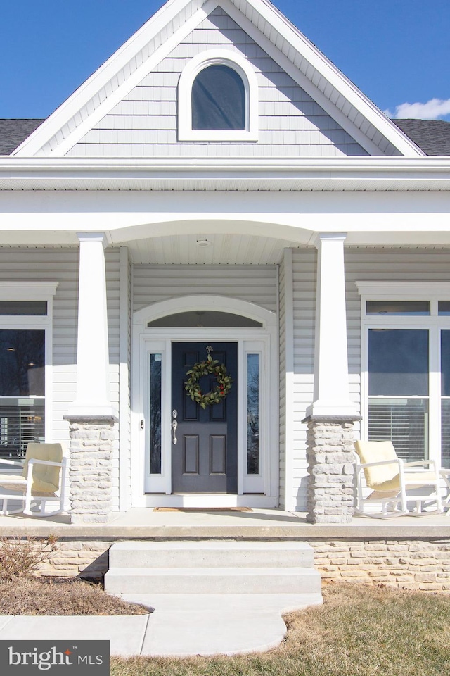 property entrance featuring covered porch and a shingled roof