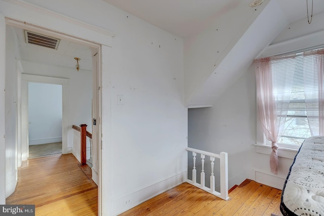 hallway featuring light wood-style flooring, visible vents, baseboards, and an upstairs landing