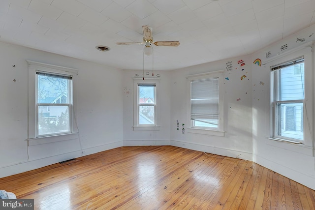 unfurnished room with a ceiling fan, light wood-type flooring, visible vents, and baseboards