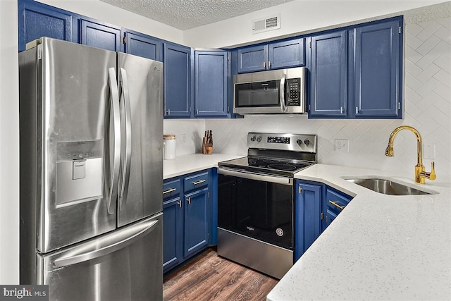 kitchen with a textured ceiling, blue cabinets, a sink, appliances with stainless steel finishes, and dark wood-style floors