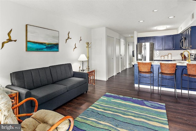 living room featuring a textured ceiling, dark wood finished floors, visible vents, and recessed lighting