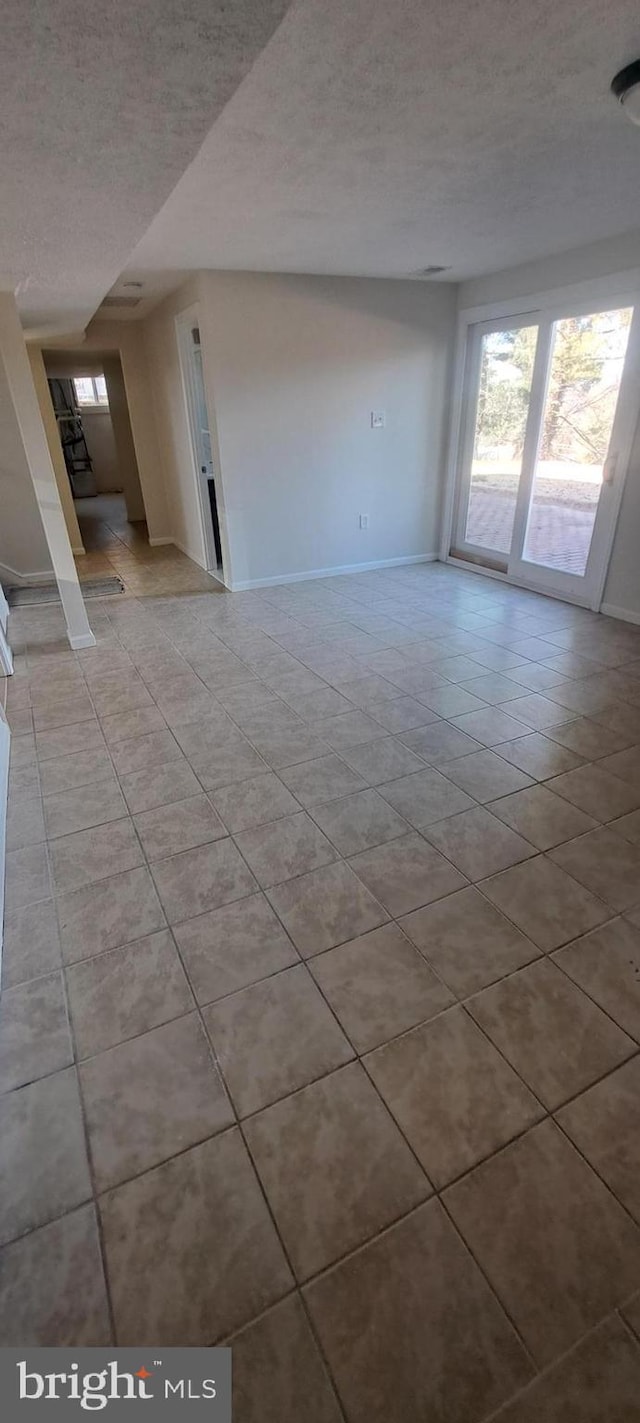 unfurnished living room with a healthy amount of sunlight, a textured ceiling, baseboards, and light tile patterned floors