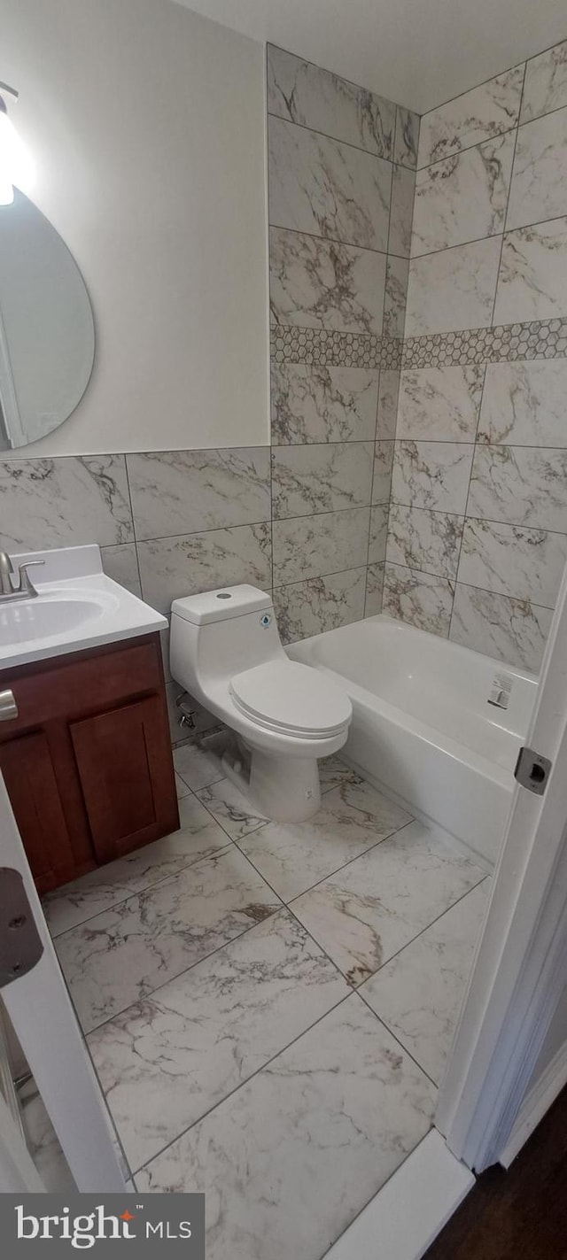 bathroom with a washtub, marble finish floor, tile walls, toilet, and vanity