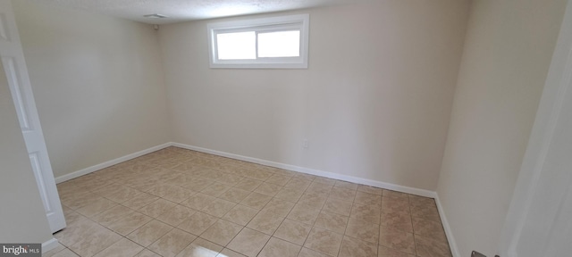 below grade area featuring light tile patterned flooring, a textured ceiling, and baseboards