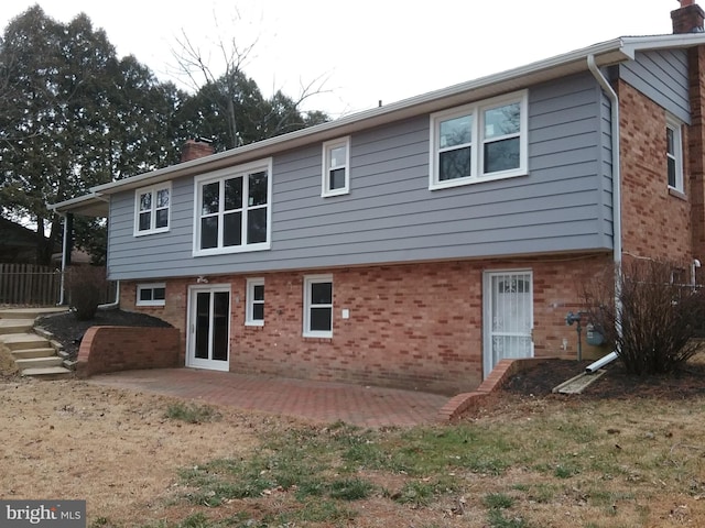 back of property with a patio area, brick siding, a chimney, and a lawn