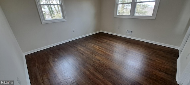 empty room featuring dark wood-style floors, baseboards, visible vents, and a wealth of natural light