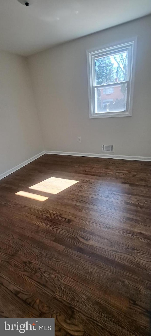 unfurnished room with dark wood-style floors, visible vents, and baseboards