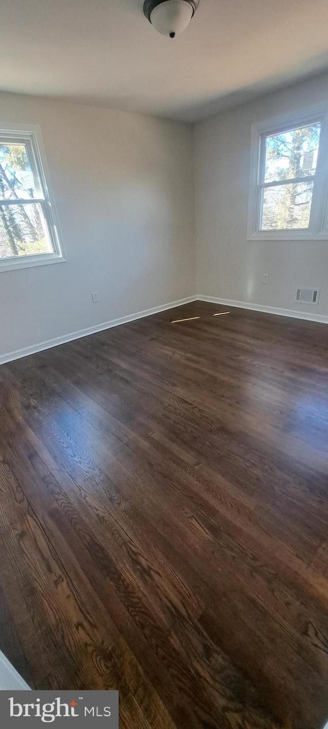 spare room featuring a healthy amount of sunlight, dark wood-style floors, baseboards, and visible vents