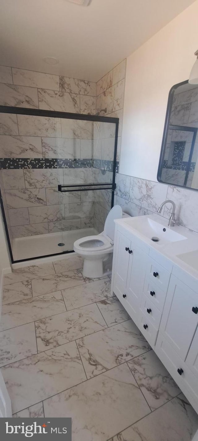 bathroom featuring toilet, a sink, marble finish floor, double vanity, and a stall shower