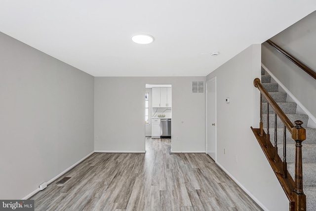 empty room featuring visible vents, light wood-style flooring, baseboards, and stairs