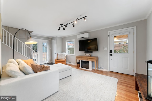 living area featuring a wall unit AC, wood finished floors, visible vents, stairs, and ornamental molding