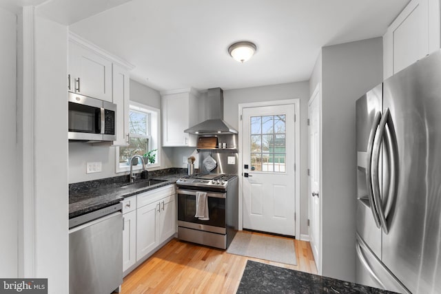 kitchen with wall chimney exhaust hood, white cabinetry, stainless steel appliances, and a sink