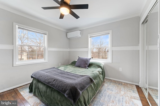 bedroom with multiple windows, a wall unit AC, wood-type flooring, and baseboards