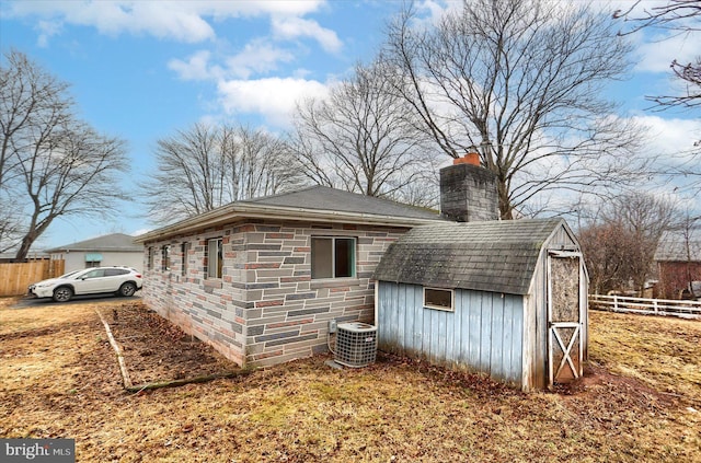 view of property exterior with stone siding, a chimney, fence, and central AC