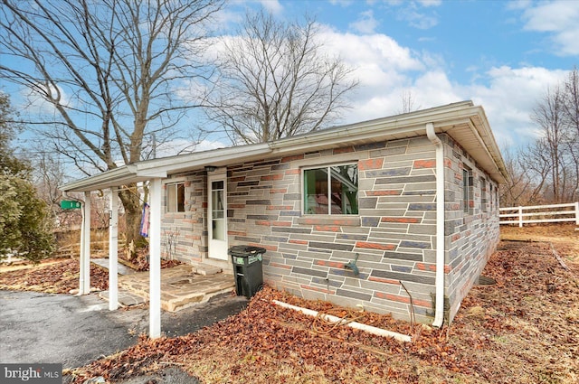 ranch-style home featuring stone siding and fence