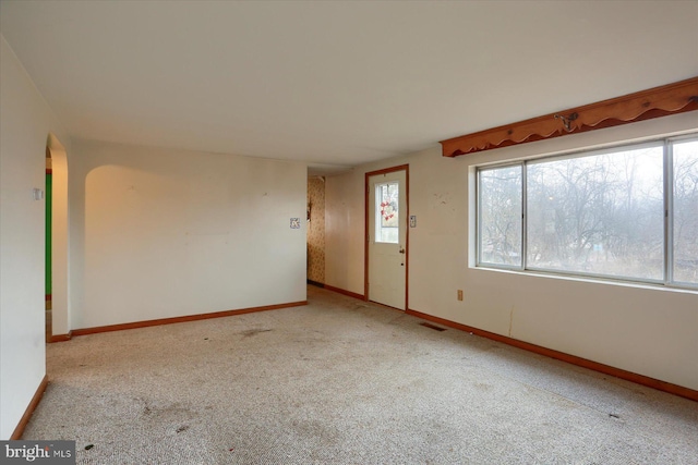 unfurnished room with carpet, visible vents, arched walkways, and baseboards