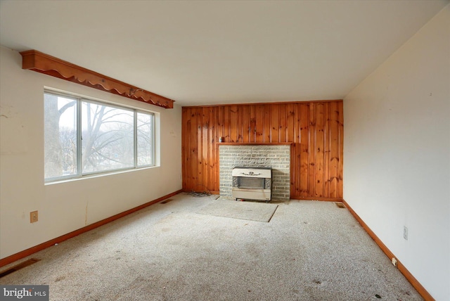 unfurnished living room featuring baseboards, carpet floors, a wood stove, and wooden walls