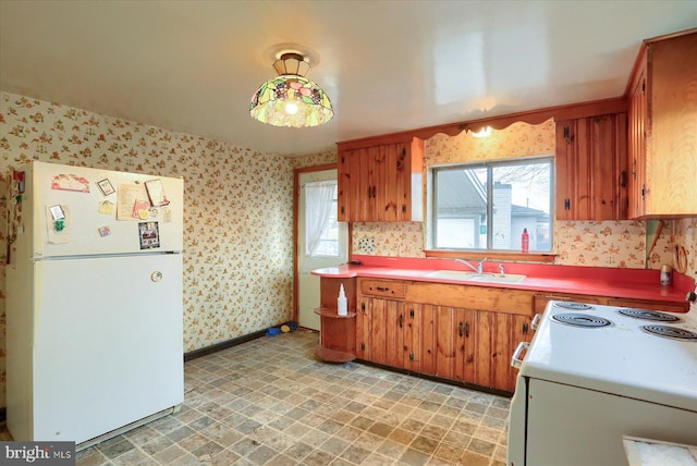 kitchen with white appliances, brown cabinets, a sink, and wallpapered walls