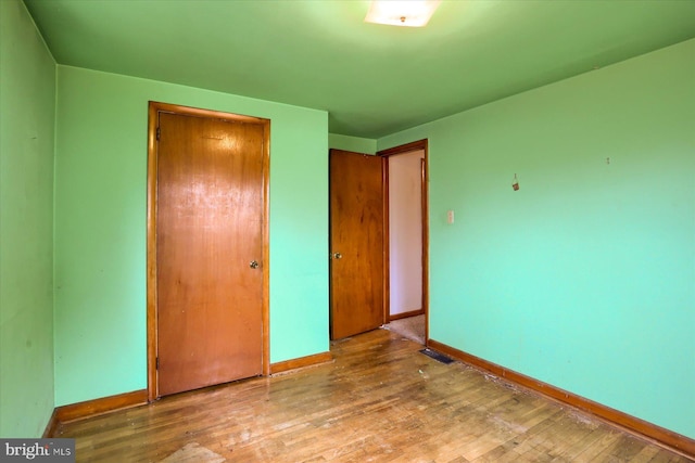 unfurnished bedroom with a closet, visible vents, wood-type flooring, and baseboards