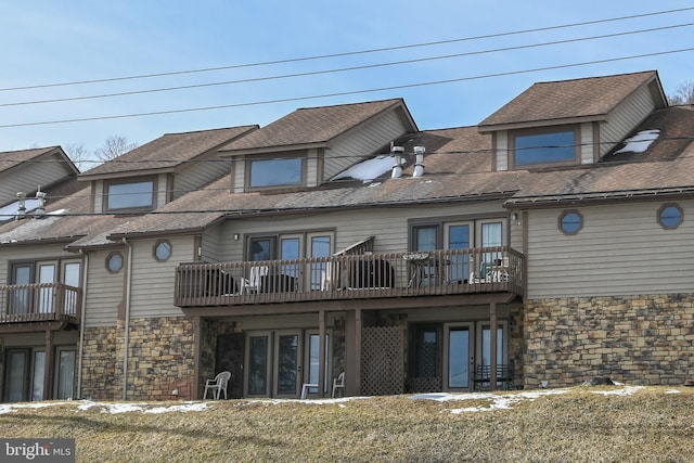 back of house featuring a yard, stone siding, and a shingled roof