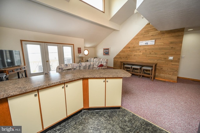 kitchen with cream cabinets, wooden walls, a peninsula, open floor plan, and dark colored carpet