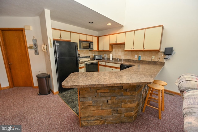 kitchen with a peninsula, cream cabinets, dark colored carpet, black appliances, and a sink