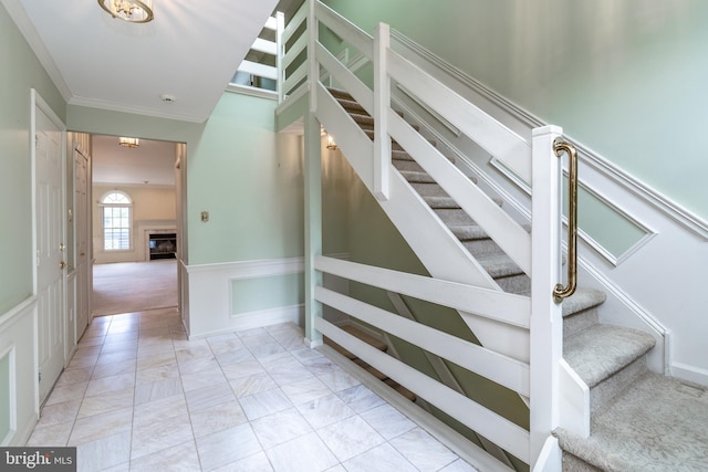 stairway with a glass covered fireplace, crown molding, carpet flooring, and a wainscoted wall