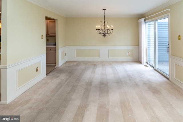 unfurnished dining area with a wainscoted wall, light colored carpet, an inviting chandelier, and ornamental molding