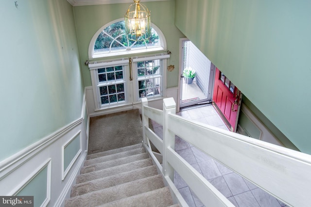 stairway with a wainscoted wall, an inviting chandelier, a high ceiling, a decorative wall, and carpet flooring