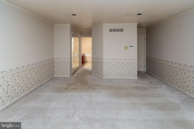 spare room featuring visible vents, wallpapered walls, a wainscoted wall, ornamental molding, and carpet floors